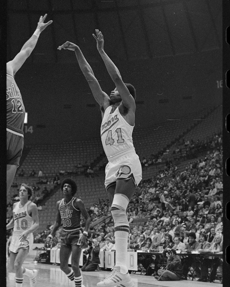 Black and white photo of Indiana Pacers player Len Elmore taking a jump shot over a defender with arms extended.